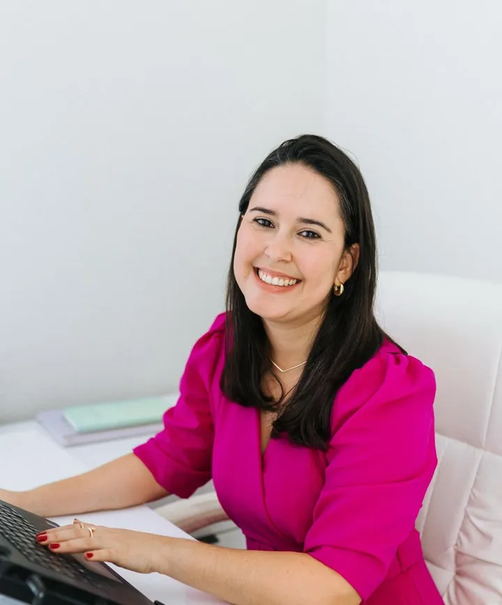 Psicóloga Clínica Lizandra Coelho sorrindo em seu consultório em Vitória enquanto usa um notebook